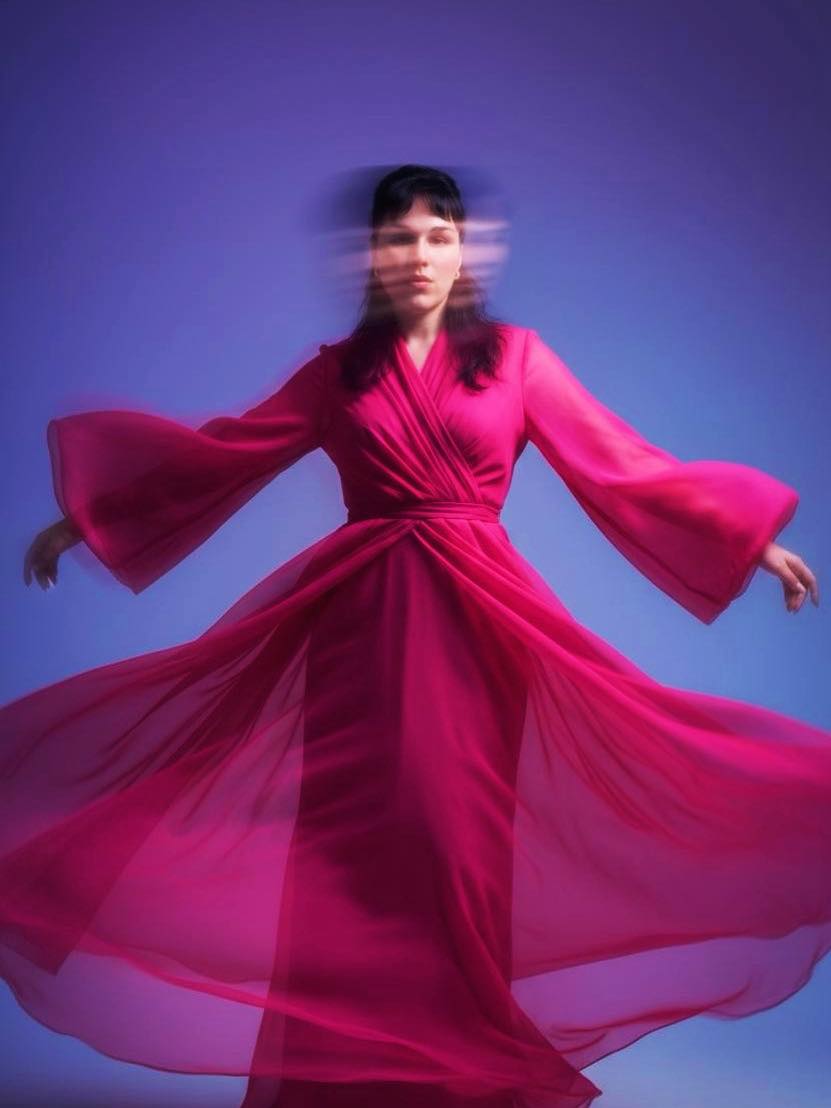 Photo en mouvement de Thamy en robe magenta, fond bleu.