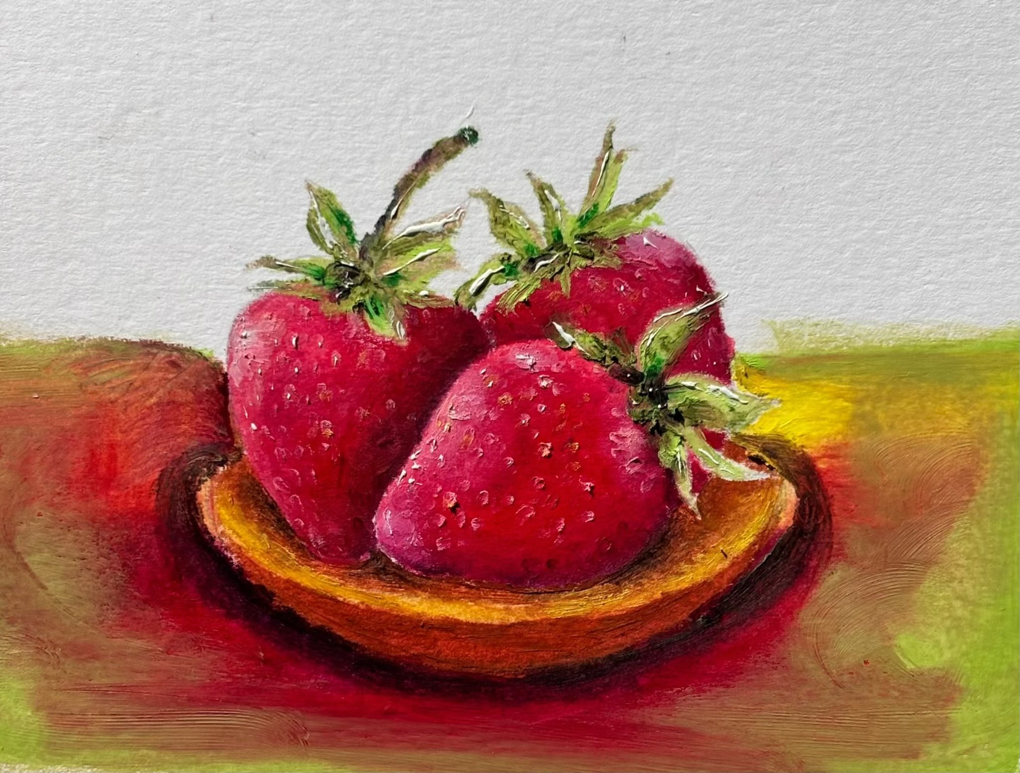 Petite huile horizontale — trois fraises rouges aux pédoncules verts dans une coupelle en bois, posée sur un fond vert et rouge.